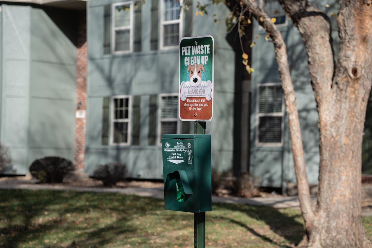 A green trash can with a sign that says "Pet Waste Pick Up" on it.